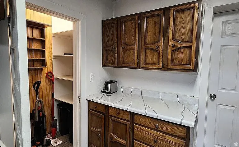 Kitchenette featuring wood-finish cabinetry, patterned countertops, and a full-height pantry with shelving