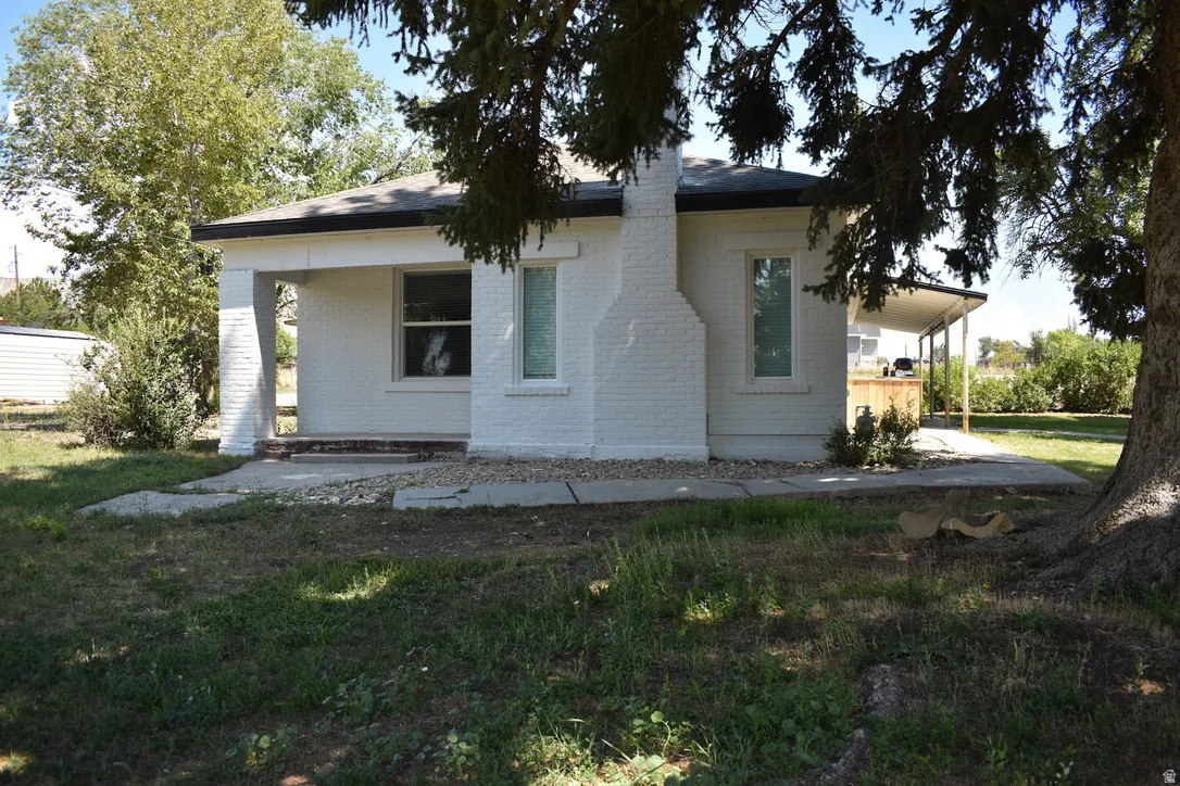 White brick exterior with a prominent brick chimney, multiple windows, and a covered front porch featuring square columns