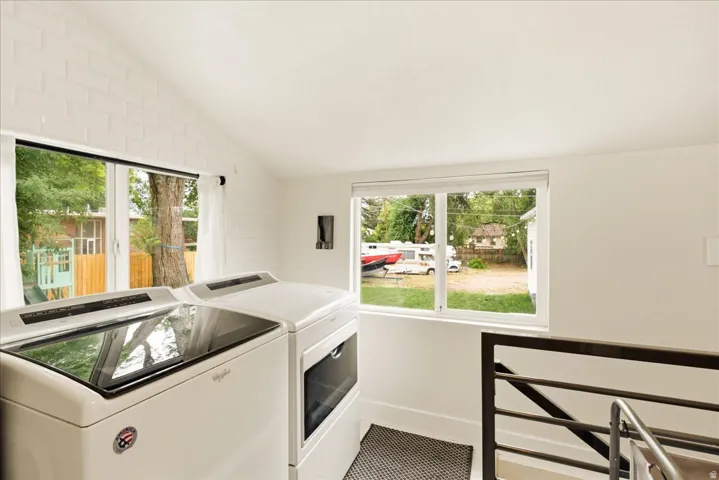 Laundry area with vaulted ceiling, white painted brick accent wall, and dual pane windows
