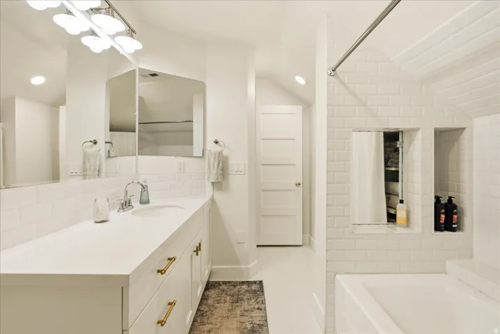 Spacious bathroom featuring a single vanity with a white countertop and gold-finish hardware, subway tile backsplash, recessed lighting, and a built-in shower niche