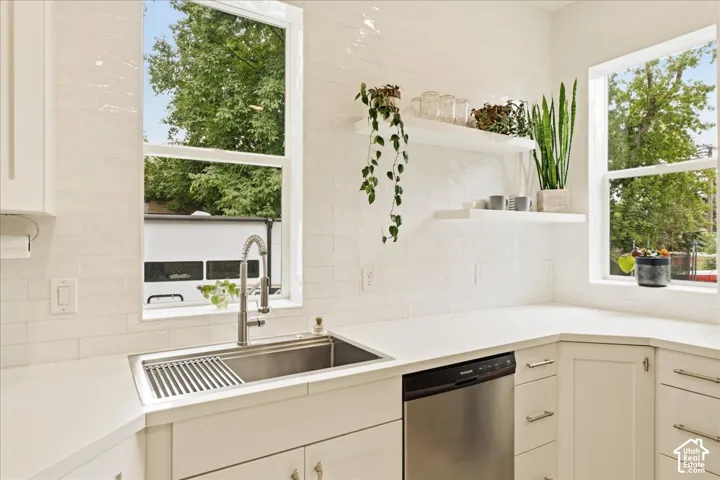 Kitchen featuring white shaker-style cabinetry, a stainless steel farmhouse sink with a gooseneck faucet, light-toned countertops, and a white subway tile backsplash