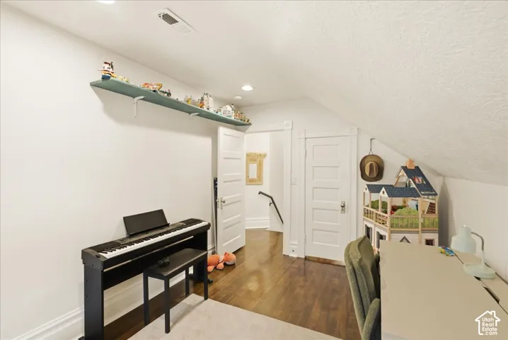 Attic room featuring rich wood-finish flooring, white walls, and a sloped ceiling