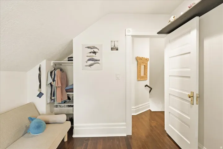 Attic room featuring rich wood-finish flooring, a built-in closet system, sloped ceiling, and white paneled door with brass hardware