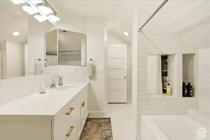 Spacious bathroom featuring a single vanity with a white countertop and gold-finish hardware, subway tile backsplash, recessed lighting, and a built-in shower niche
