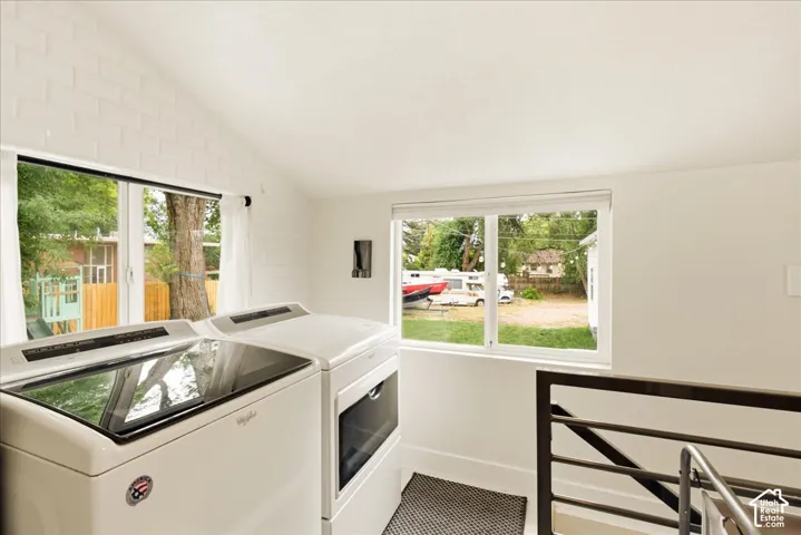 Laundry area with vaulted ceiling, white painted brick accent wall, and dual pane windows