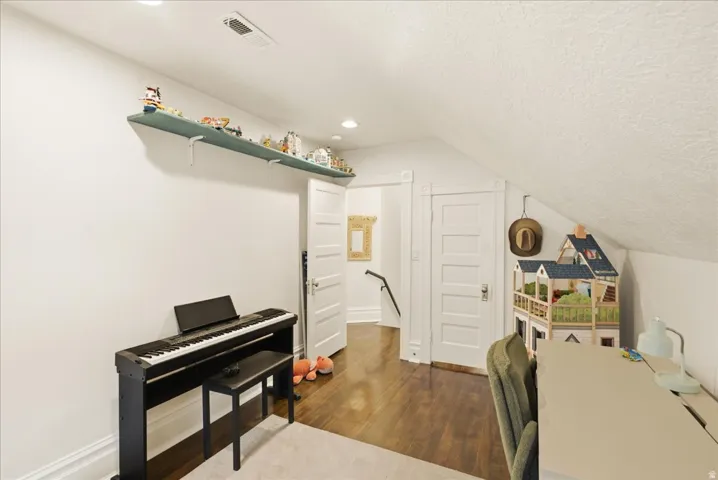 Attic room featuring rich wood-finish flooring, white walls, and a sloped ceiling