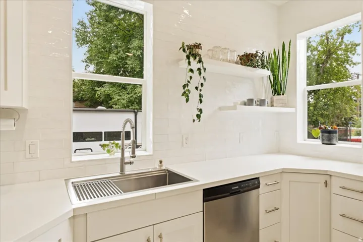 Kitchen featuring white shaker-style cabinetry, a stainless steel farmhouse sink with a gooseneck faucet, light-toned countertops, and a white subway tile backsplash