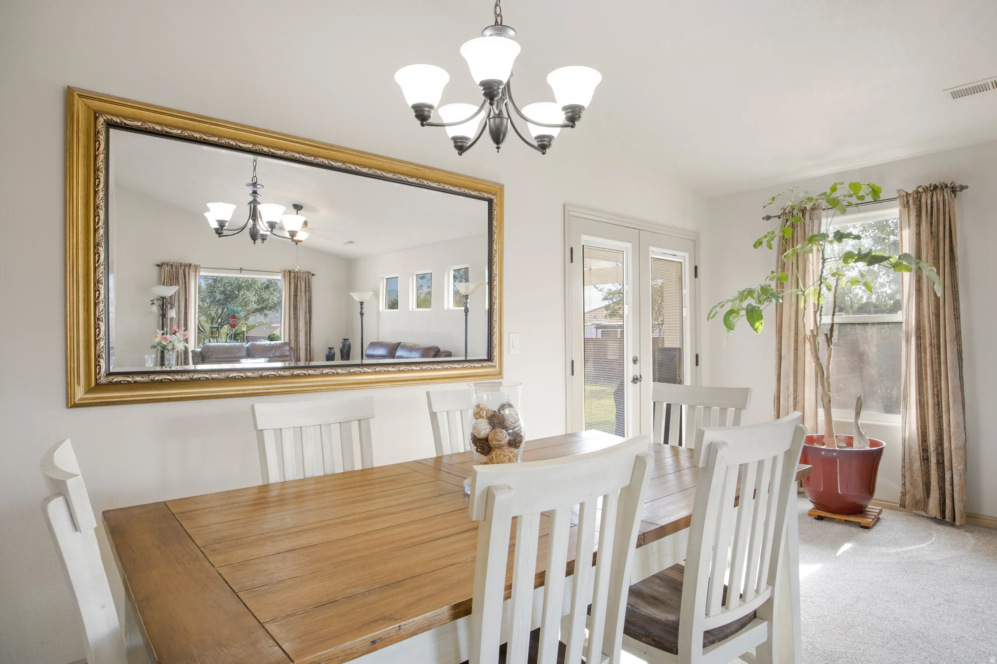 Dining area featuring a contemporary chandelier, large wall-mounted mirror with an ornate gold frame, and light-tone wood-finish flooring