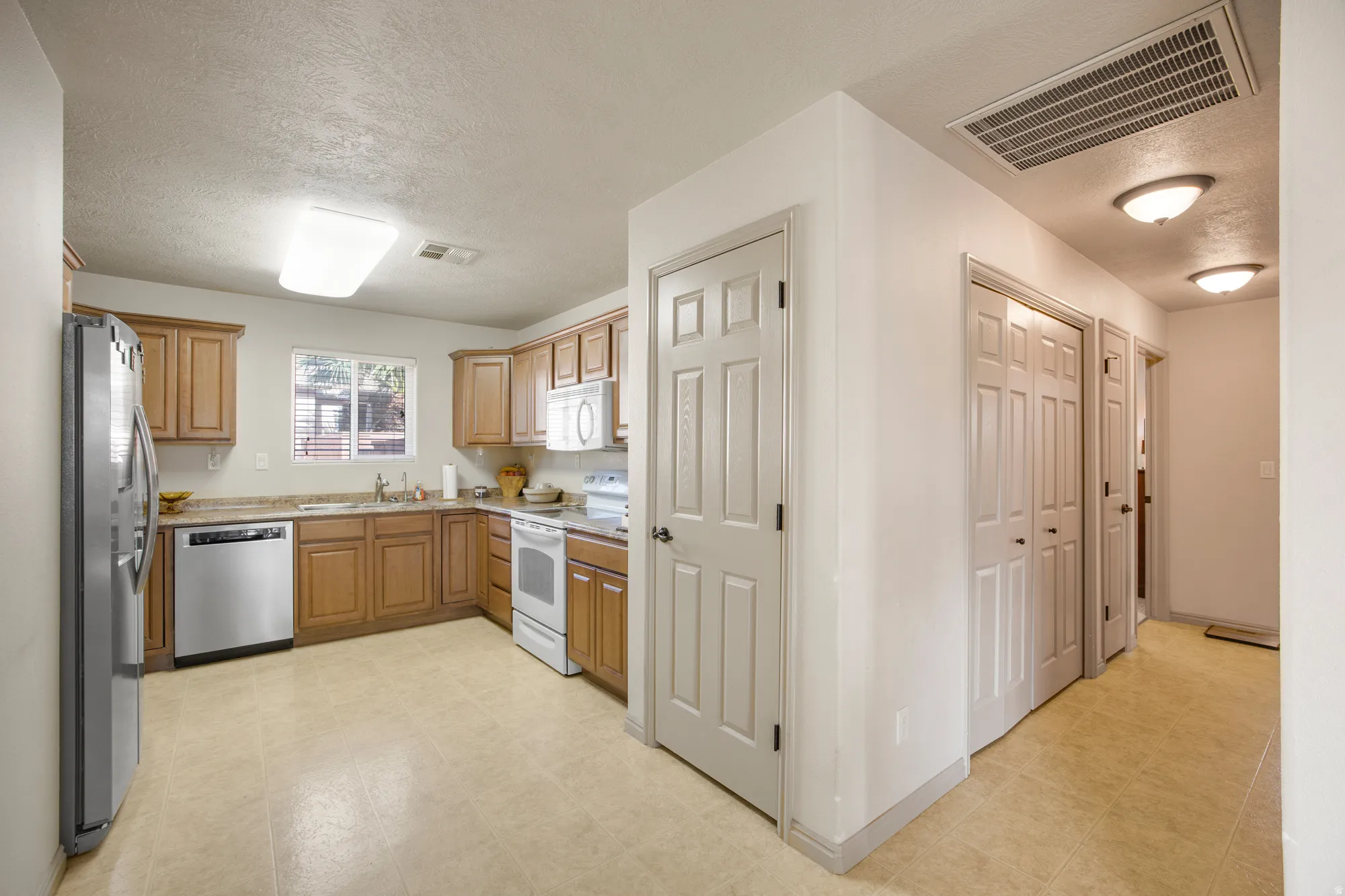 Functional kitchen with wood-finish cabinetry, light-toned countertops, a stainless steel refrigerator, and integrated dishwasher