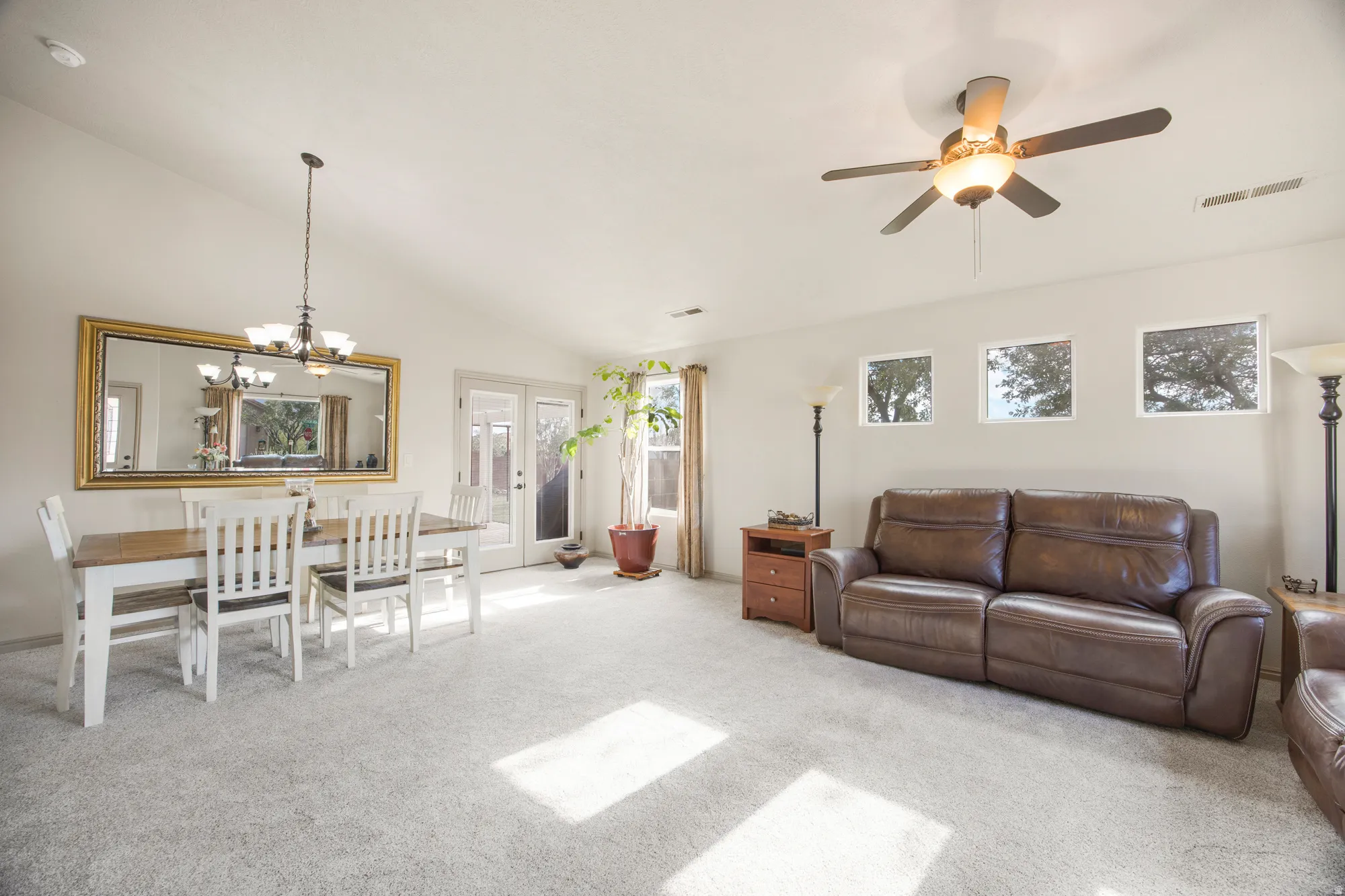Open-concept living space featuring vaulted ceilings, a ceiling fan with integrated lighting, and light-toned carpeting