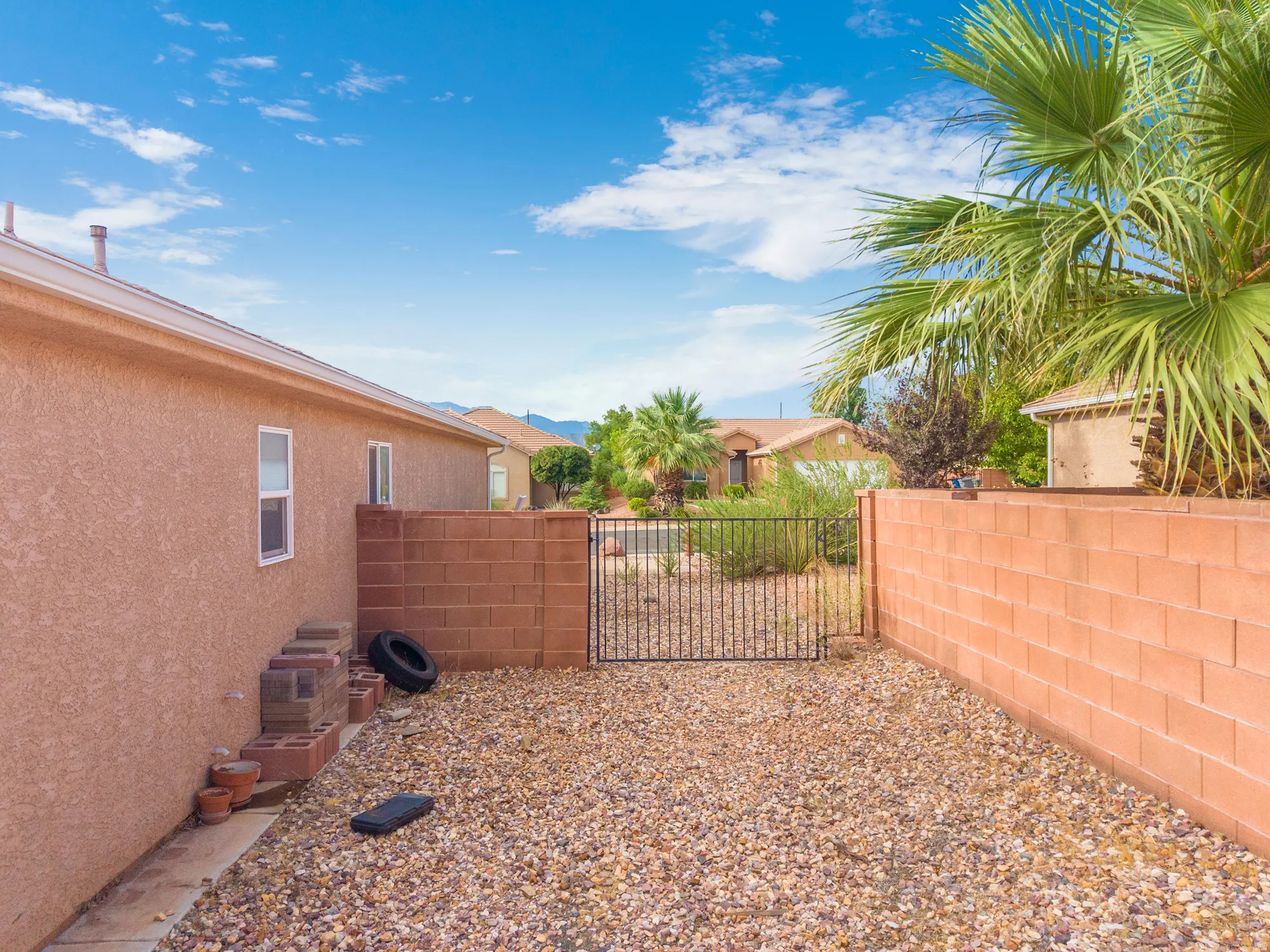 Gravel yard featuring a block wall, wrought iron gate, and stucco exterior