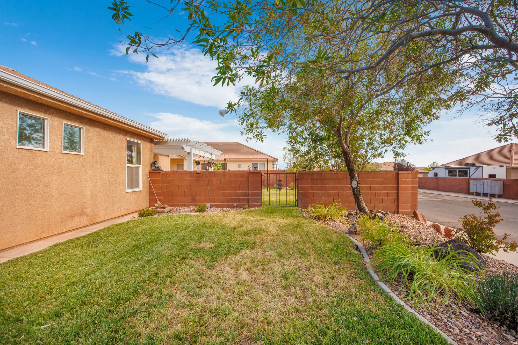 Expansive grassy yard area featuring a mature tree, a red brick perimeter wall, and a wrought iron gate