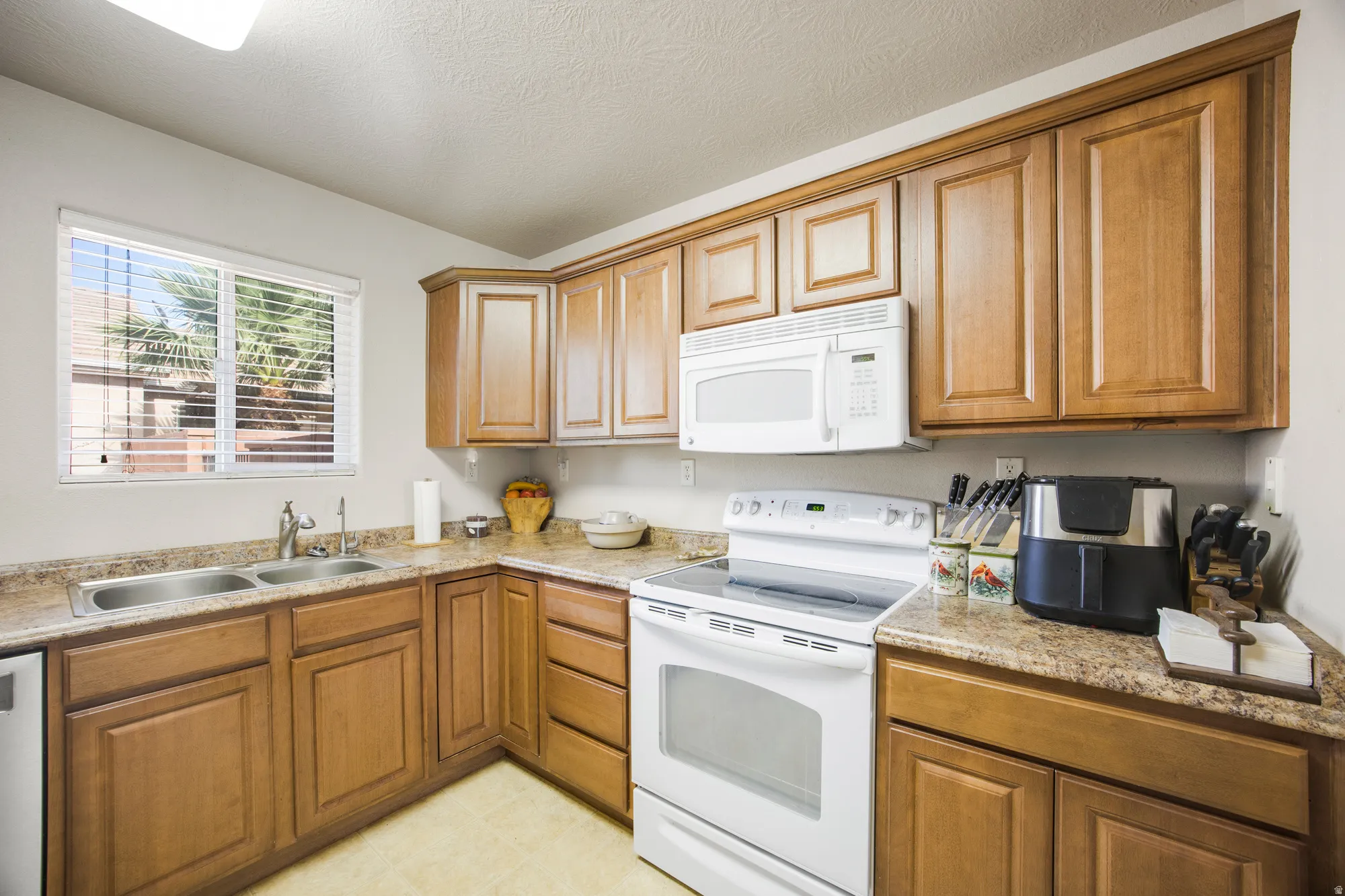Kitchen featuring wood-finish cabinetry, light-toned countertops, and a double basin stainless steel sink