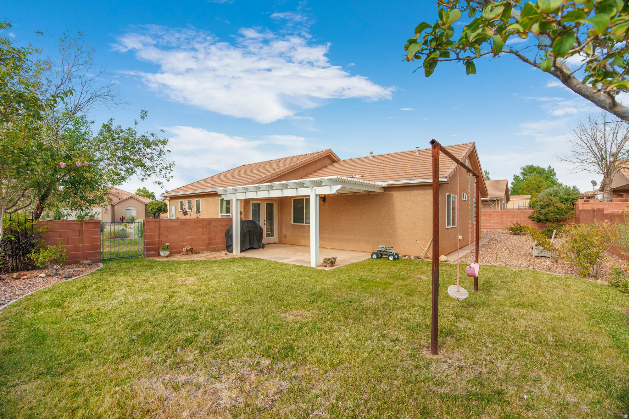 Spacious backyard featuring a covered patio, extensive lawn, block wall fencing, and double glass doors