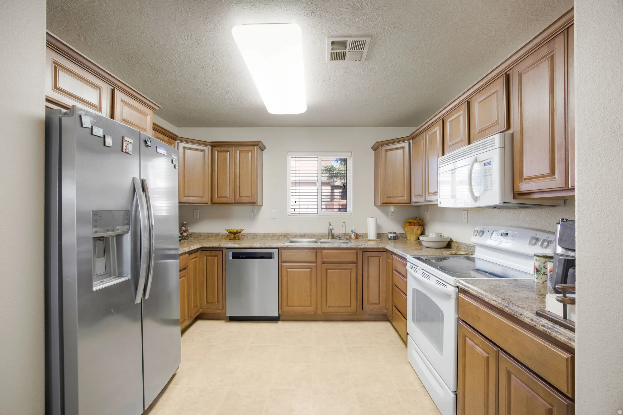 Well-appointed kitchen featuring light wood cabinetry, stone countertops, stainless steel refrigerator, stainless steel dishwasher, and a built-in microwave