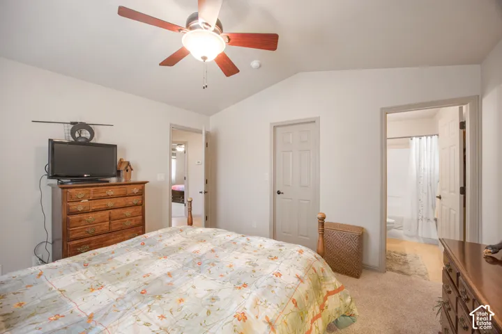 Vaulted ceiling with a ceiling fan light fixture, neutral wall paint, and soft carpet flooring
