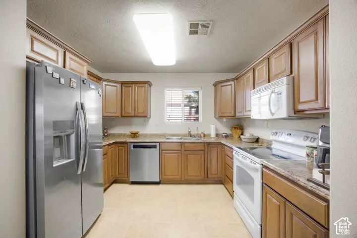 Well-appointed kitchen featuring light wood cabinetry, stone countertops, stainless steel refrigerator, stainless steel dishwasher, and a built-in microwave