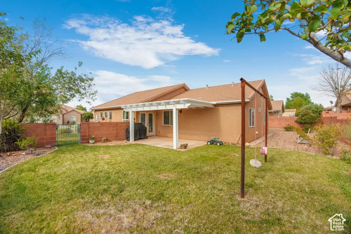 Spacious backyard featuring a covered patio, extensive lawn, block wall fencing, and double glass doors
