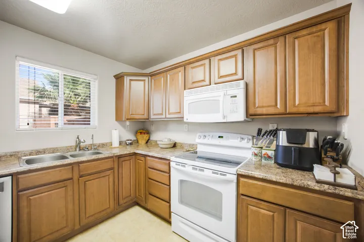 Kitchen featuring wood-finish cabinetry, light-toned countertops, and a double basin stainless steel sink