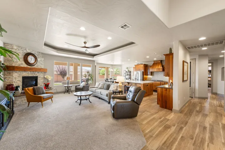 Expansive open-concept interior featuring a stone fireplace with a wood mantle, a tray ceiling with recessed lighting, and a ceiling fan