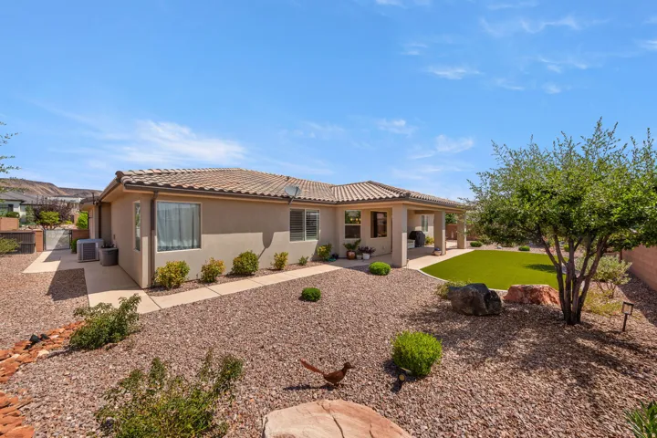 Rear exterior featuring a covered patio, extensive gravel landscaping, and a section of artificial turf