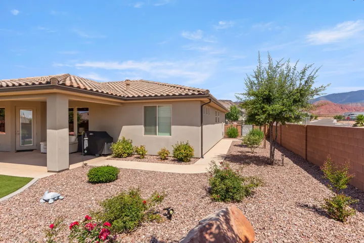 Exterior stucco siding featuring a covered patio, tile roofing, and a low-maintenance landscape