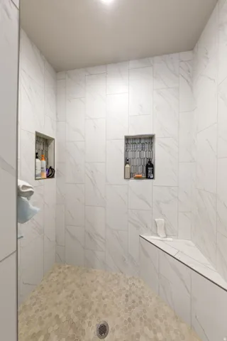 Spacious shower featuring white marble-look wall tiles, hexagonal floor tiles, two recessed niches, and a built-in bench