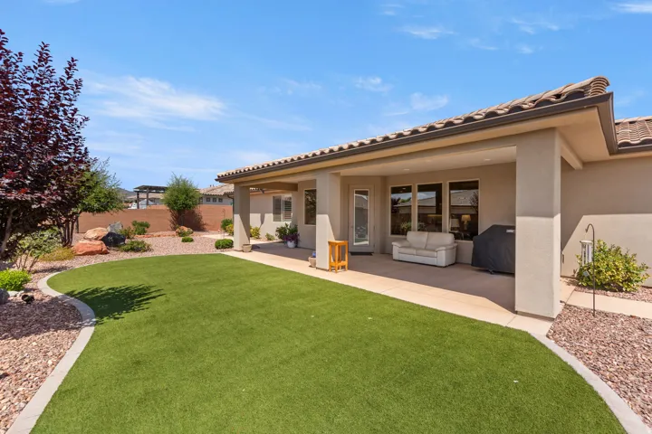 Expansive outdoor living space featuring a covered patio, artificial turf lawn, desert landscaping with decorative rocks, and mature shrubs