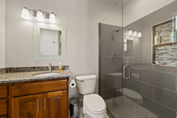 Walk-in shower featuring a glass enclosure, built-in shelving with mosaic tile, and a rainfall showerhead