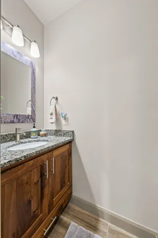 Vanity featuring a stone countertop, an undermount sink, and wood-finish cabinetry with silver hardware