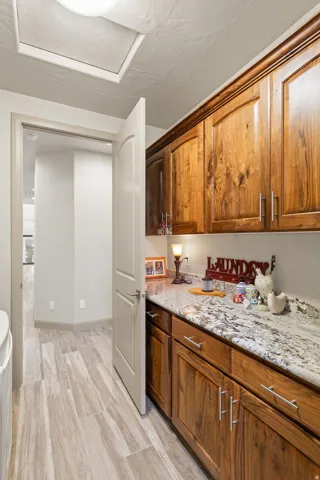Laundry area featuring wood-finish cabinetry, granite-style countertops, wood-look flooring, recessed lighting, and a white interior door