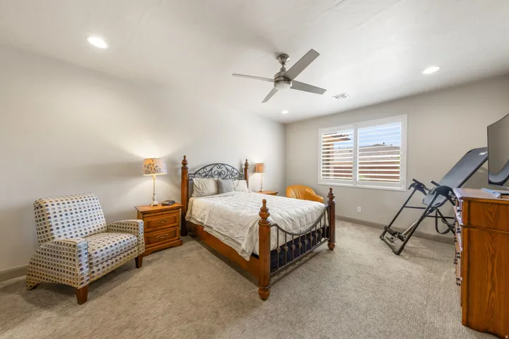 Carpeted bedroom featuring a ceiling fan with integrated lighting, recessed lighting, and a window with plantation shutters