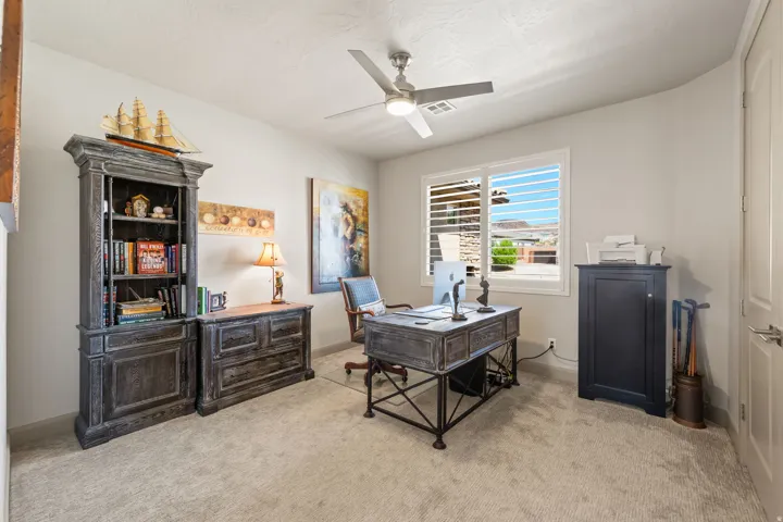 Light-filled room featuring a window with plantation shutters, neutral carpeting, a ceiling fan, and a light-toned wall finish