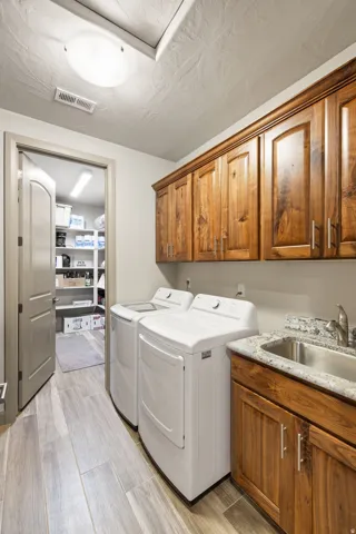 Laundry room featuring wood-finish flooring, overhead cabinetry, a utility sink with a stone-finish countertop, and a built-in light fixture