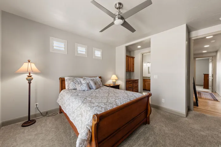 Carpeted room featuring a ceiling fan with integrated lighting, three transom windows, and a doorway opening to a hall with wood-finish flooring