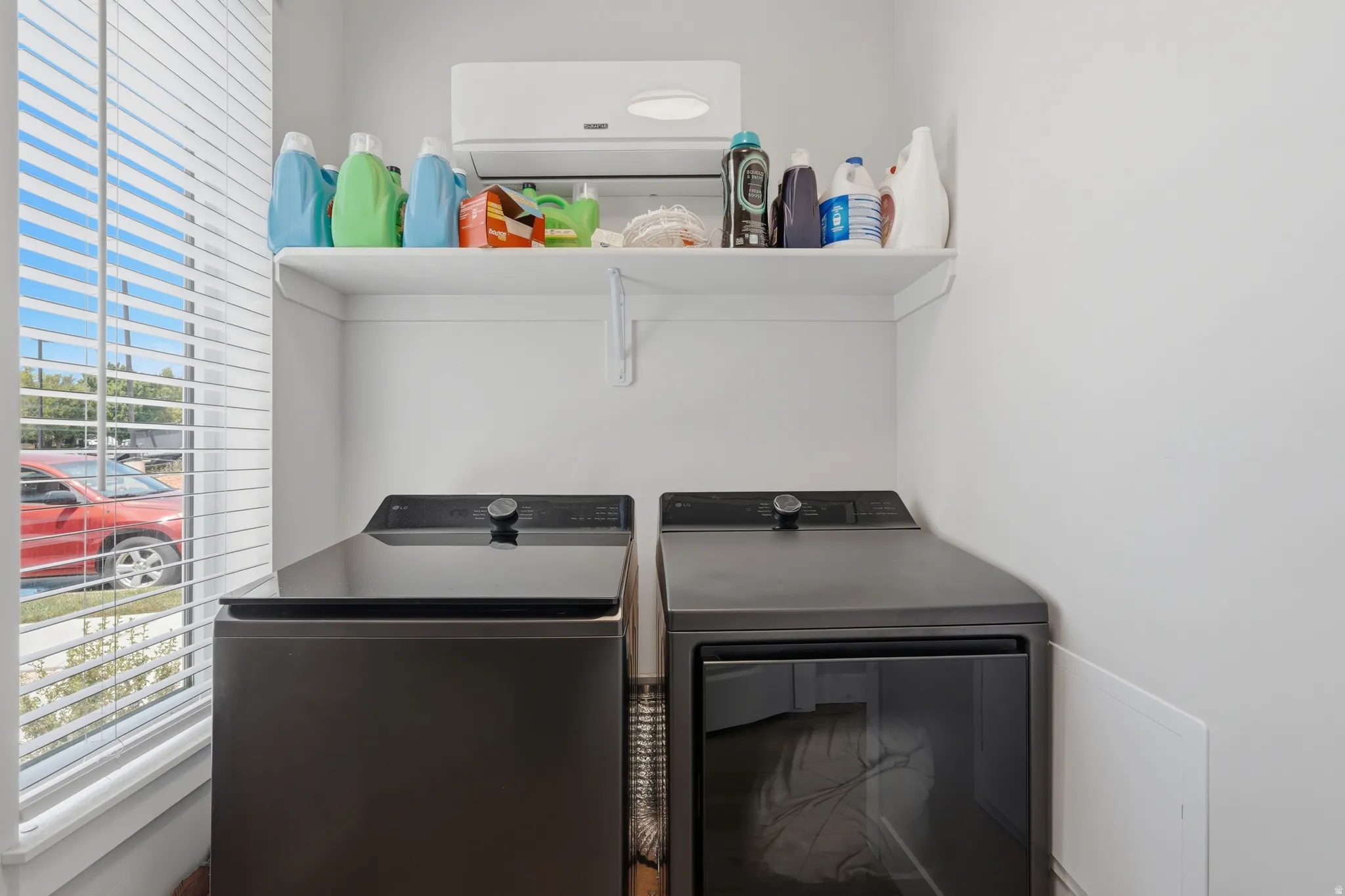 Dedicated laundry area with a white shelving unit, light-toned walls, and a window featuring horizontal blinds