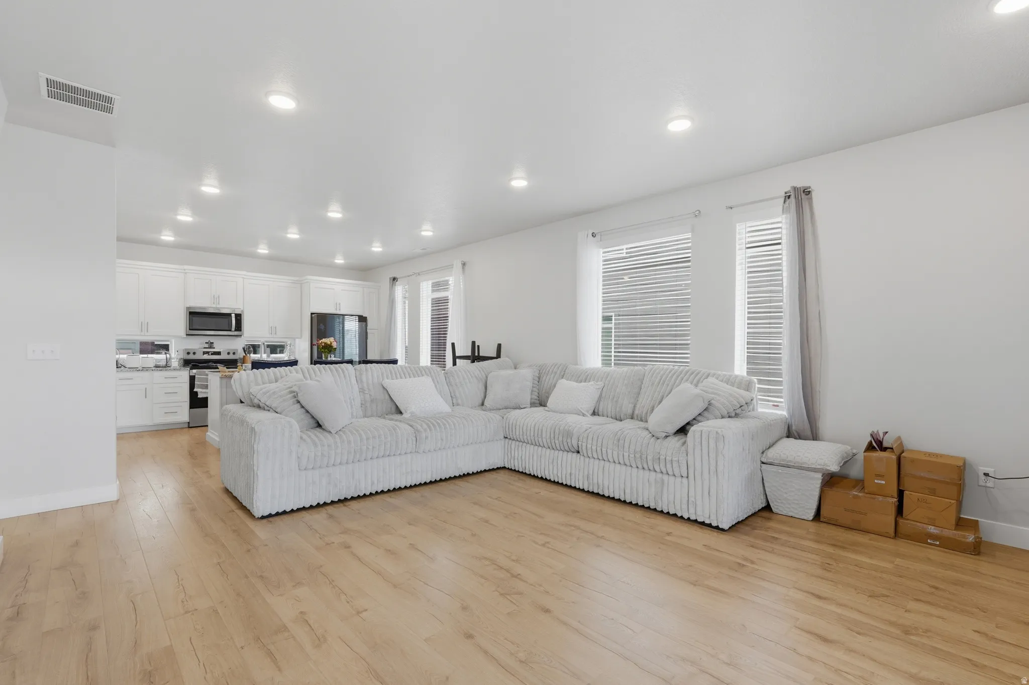 Open-concept living area featuring light wood-finish flooring, recessed lighting, and multiple windows with blinds