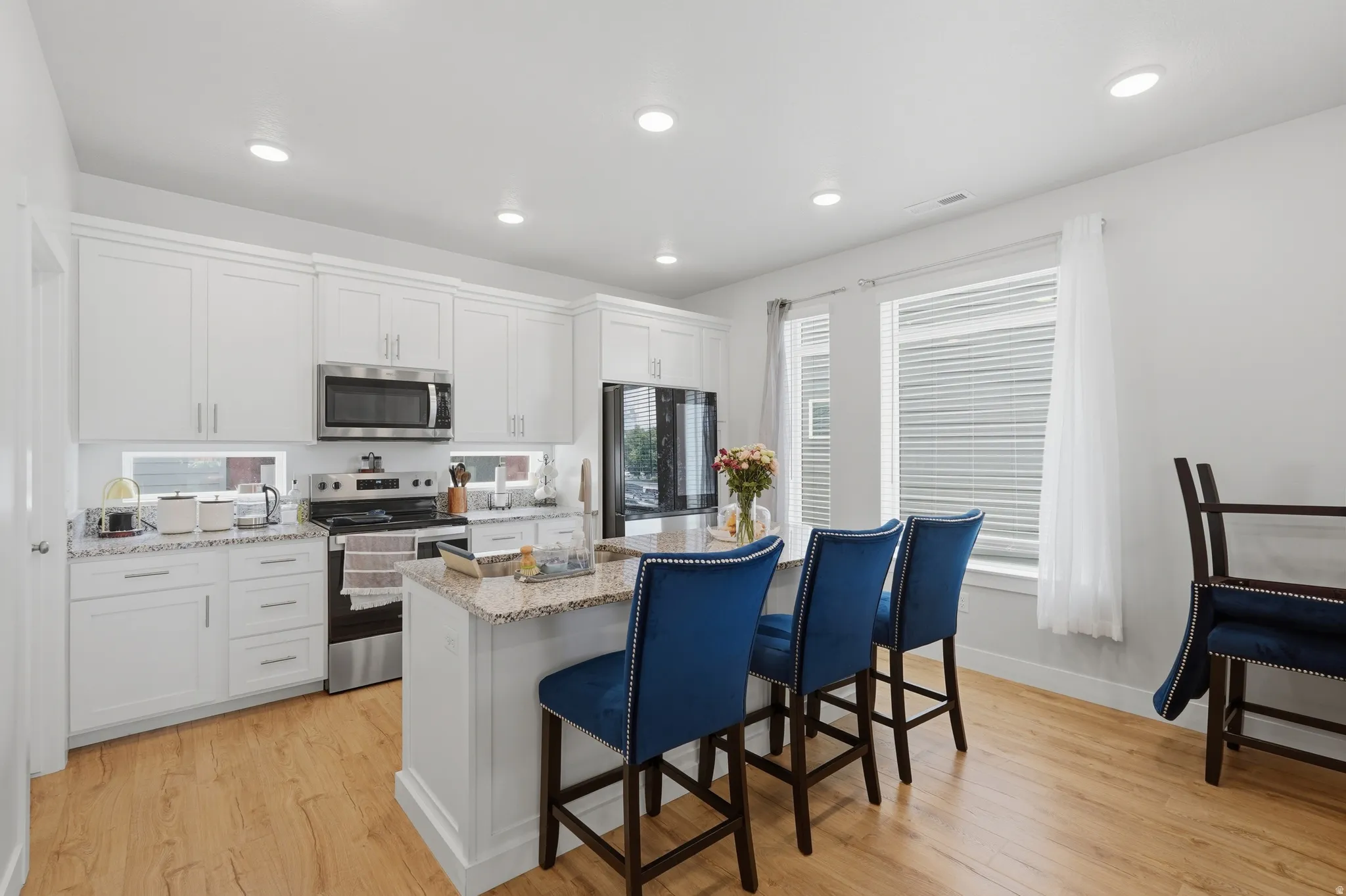 Kitchen featuring white cabinetry, stainless steel appliances, recessed lighting, a central island with a stone countertop, and wood-finish flooring