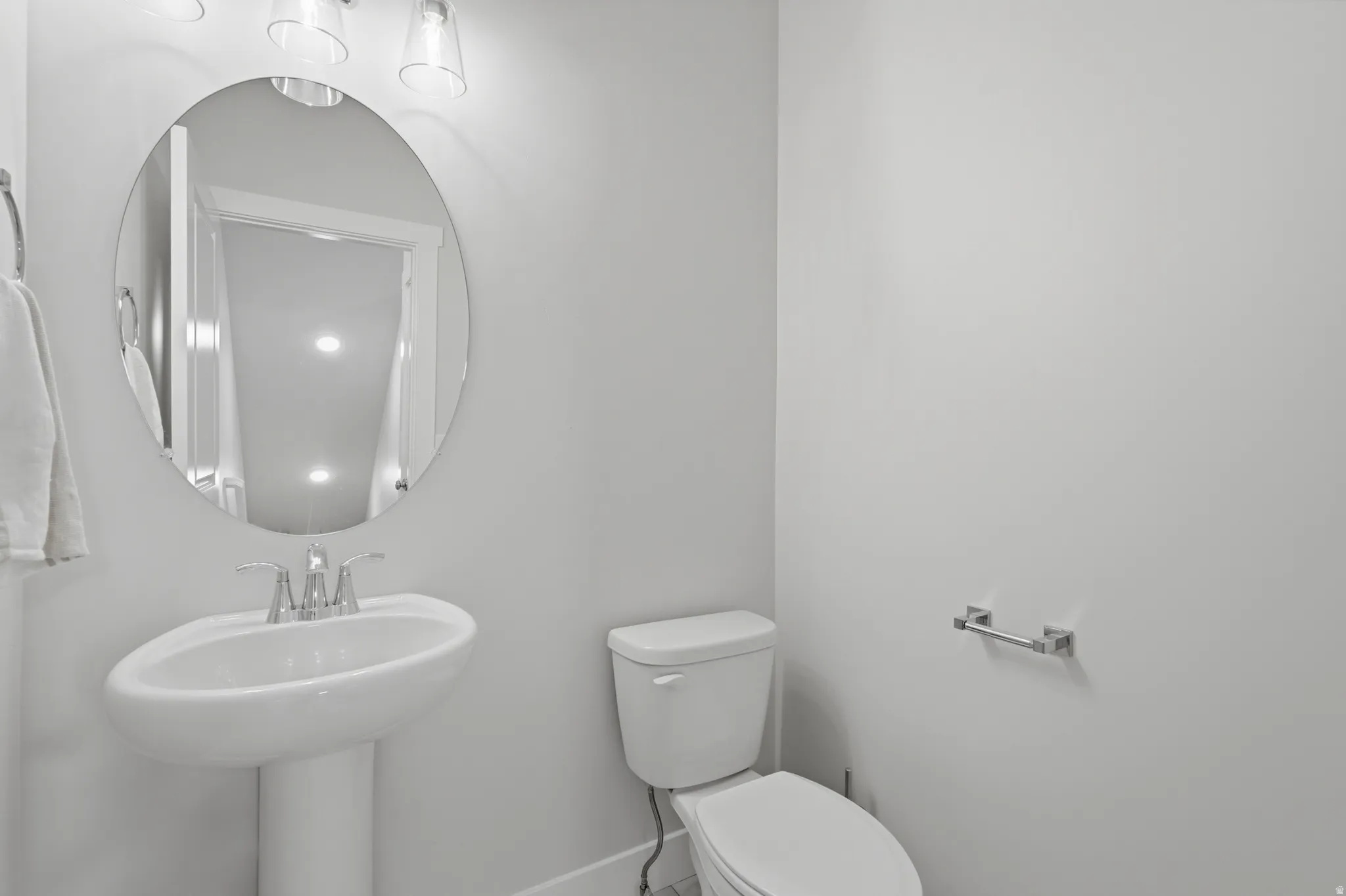 Pedestal sink featuring chrome fixtures, an oval mirror, and a three-light vanity fixture
