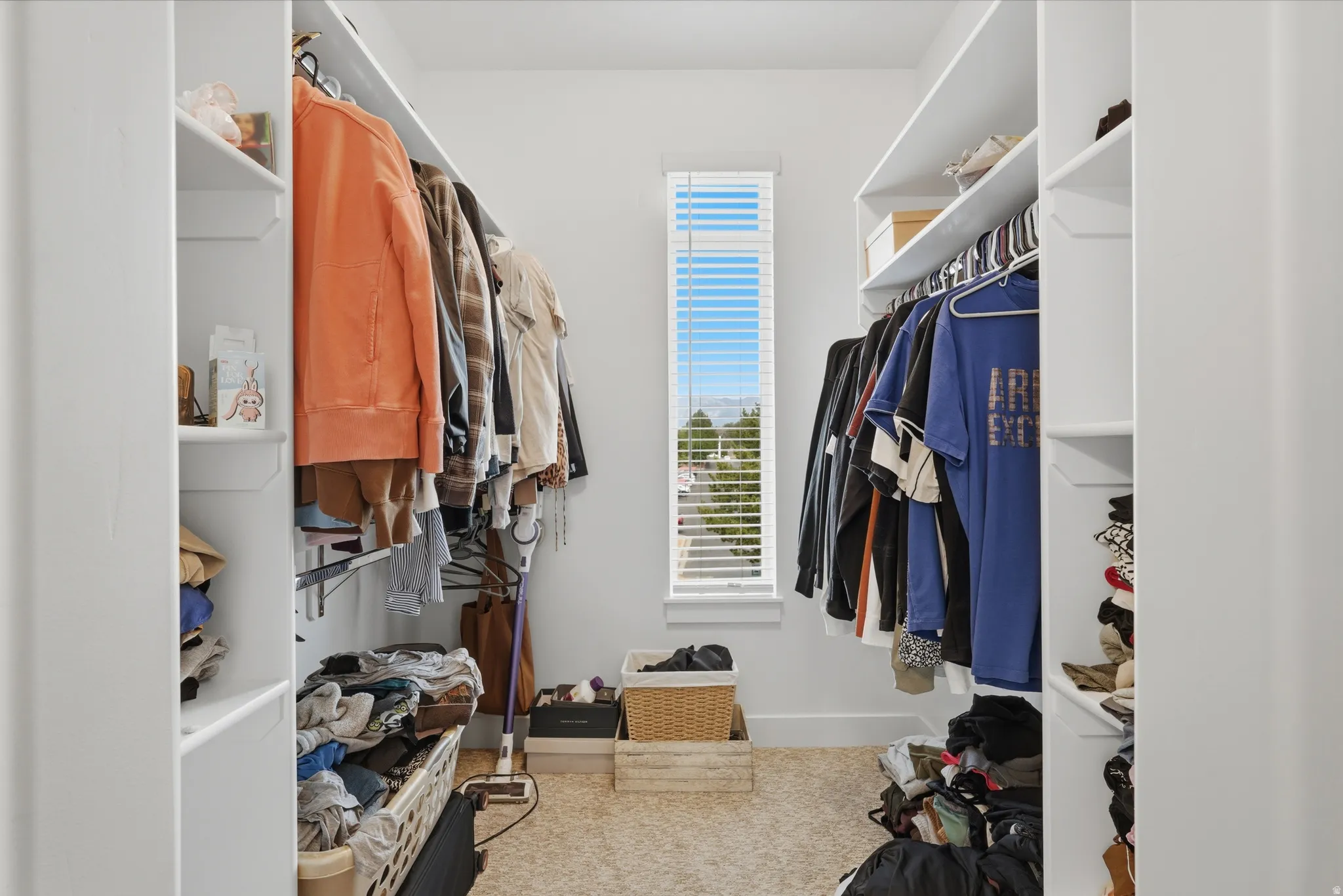 Walk-in closet with ample storage, featuring built-in shelving, hanging rods, and a tall window with horizontal blinds