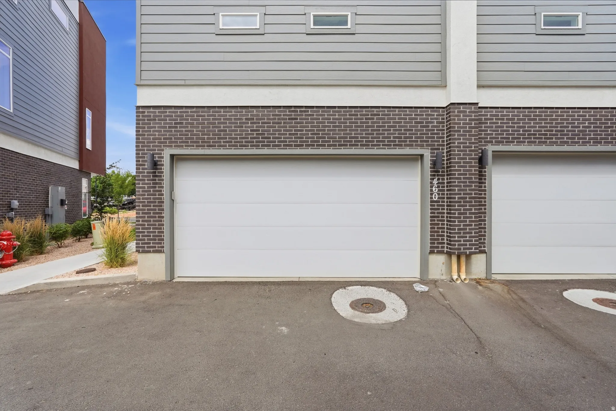 Modern townhouse exterior featuring a white garage door, dark brick facade, horizontal gray siding, and narrow rectangular windows