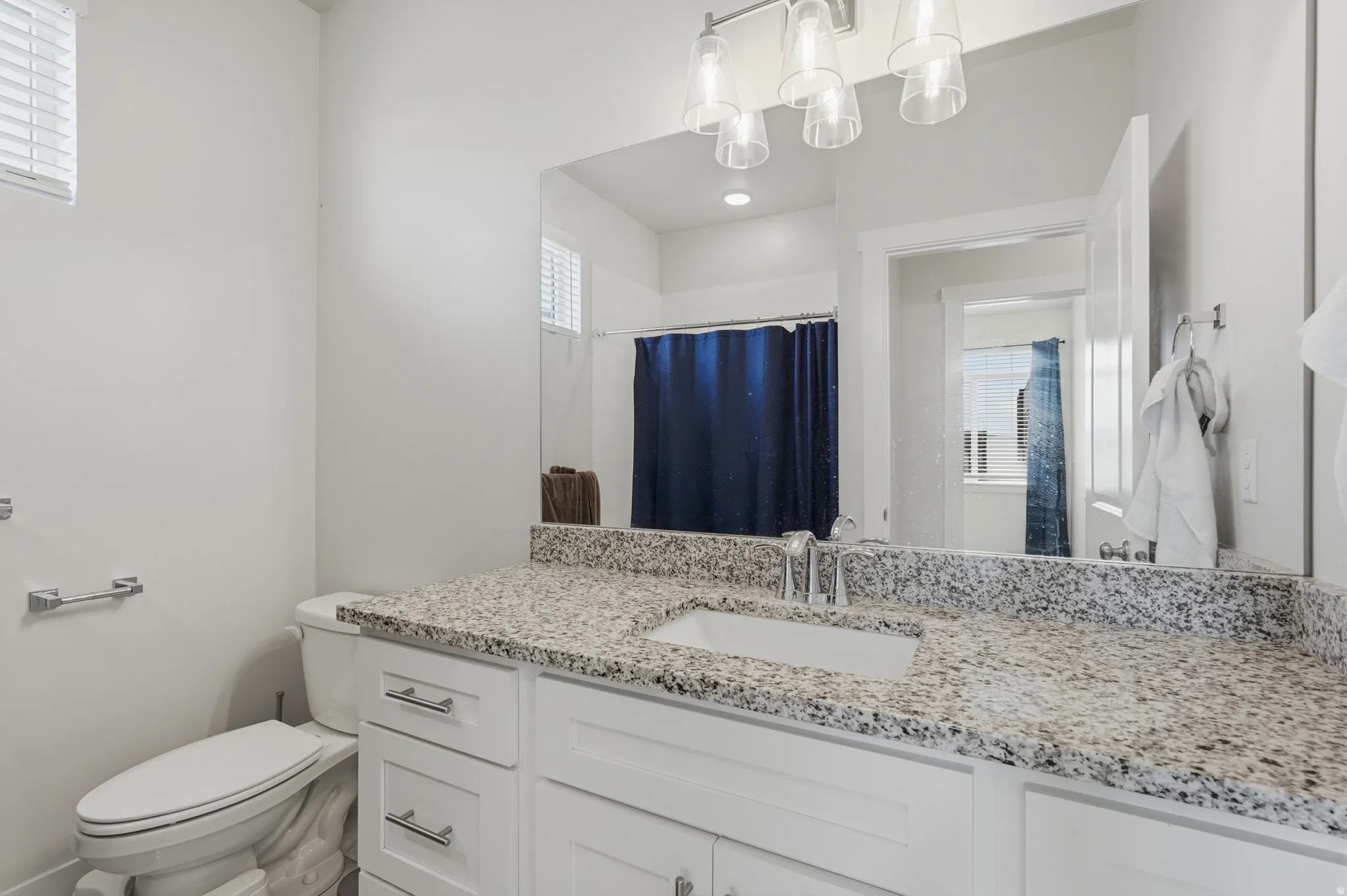 Bathroom vanity featuring a light-toned granite countertop with an undermount sink, white cabinetry with silver-tone hardware, and a large wall-mounted mirror
