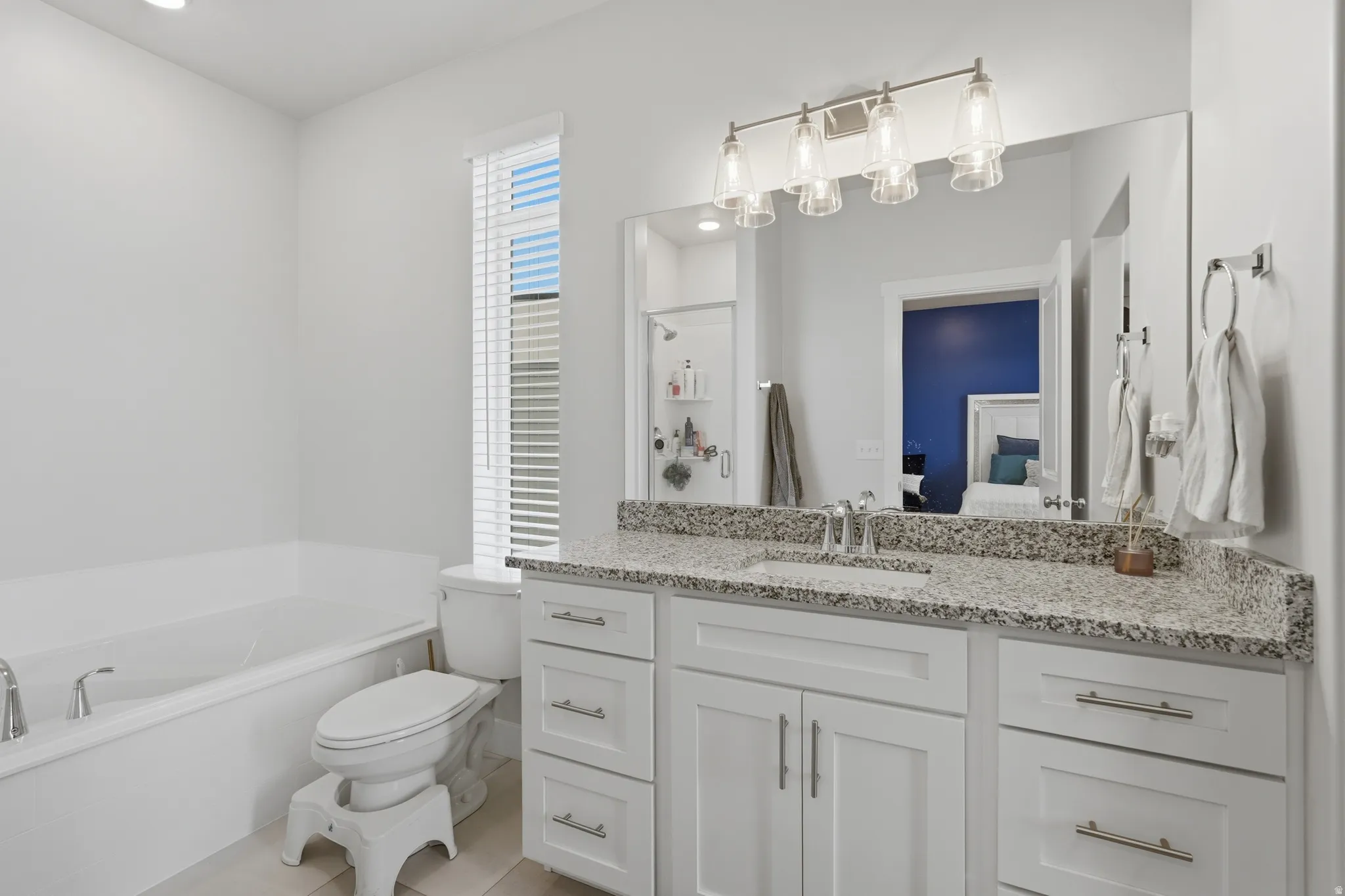 Bathroom featuring a freestanding soaking tub, a single vanity with stone countertop, white shaker cabinetry, and a brushed nickel light fixture