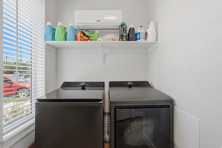 Dedicated laundry area with a white shelving unit, light-toned walls, and a window featuring horizontal blinds