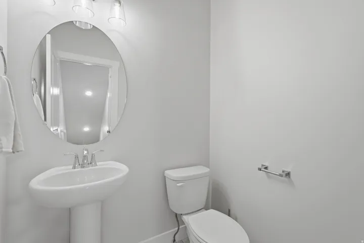 Pedestal sink featuring chrome fixtures, an oval mirror, and a three-light vanity fixture