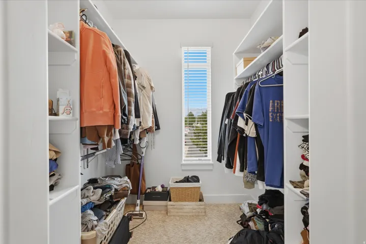 Walk-in closet with ample storage, featuring built-in shelving, hanging rods, and a tall window with horizontal blinds