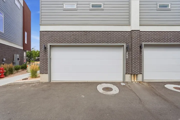 Modern townhouse exterior featuring a white garage door, dark brick facade, horizontal gray siding, and narrow rectangular windows