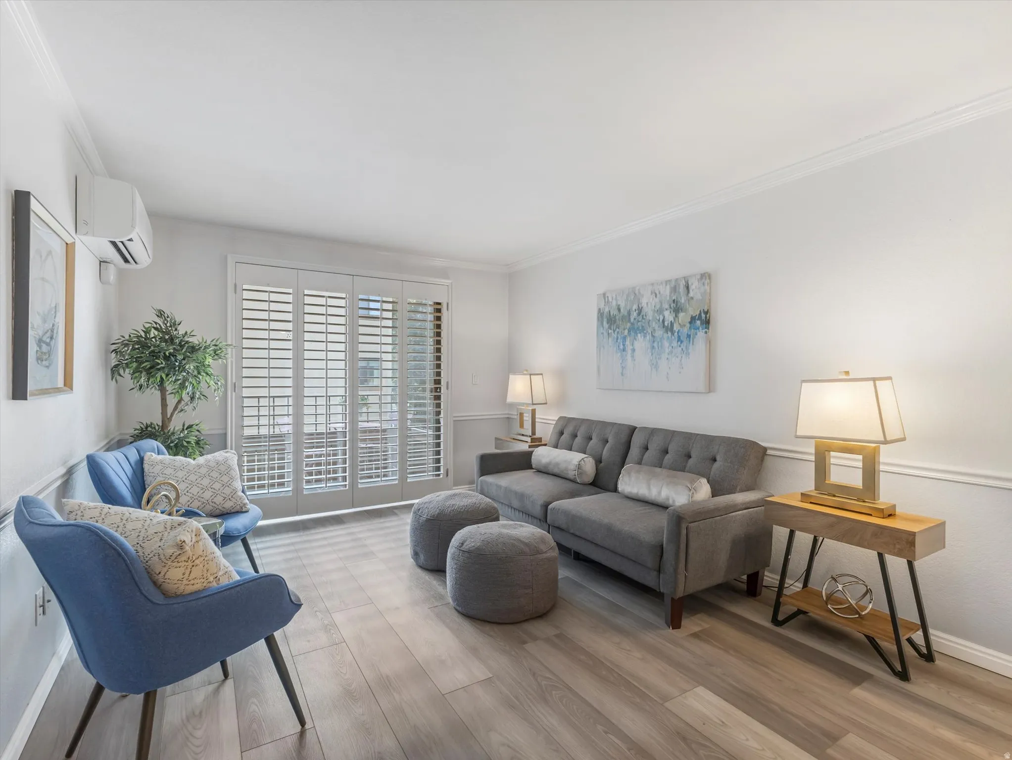 Living area featuring wood-finish flooring, white walls with crown molding, and sliding glass doors with plantation shutters