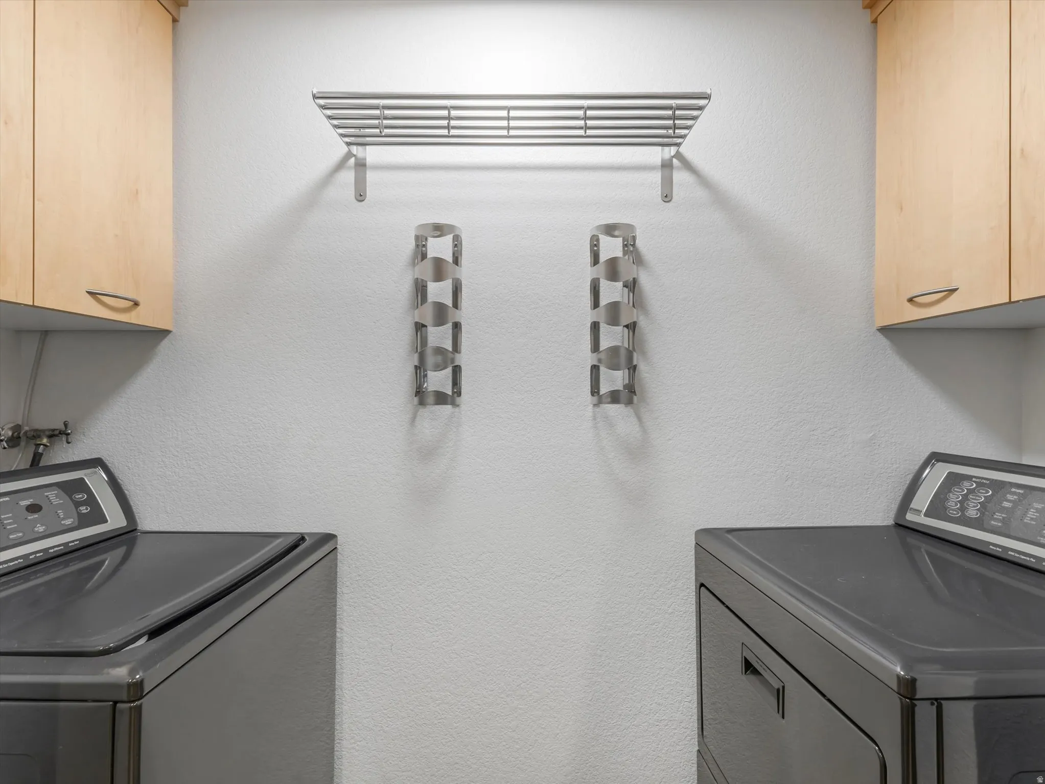 Laundry area featuring light wood-finish cabinetry, a wall-mounted drying rack, and two wall-mounted storage units