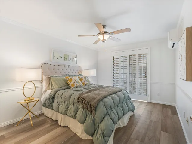 Bedroom with wood-finish flooring, white wainscoting, crown molding, and a ceiling fan